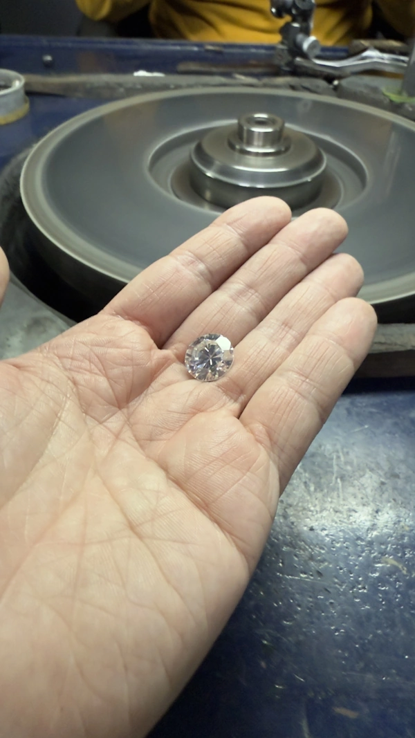 A large round brilliant diamond in hand at the cutting wheel.